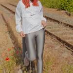 red haired girl standing in front of a post wearing a shiny nylon nike windbreaker jacket and glossy shiny silver spandex leggings