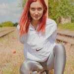 red haired girl kneeling in front of a post wearing a shiny nylon nike windbreaker jacket and glossy shiny silver spandex leggings