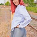 red haired showing her backside, looking to the camera, wearing a shiny nylon nike windbreaker jacket and glossy shiny silver spandex leggings